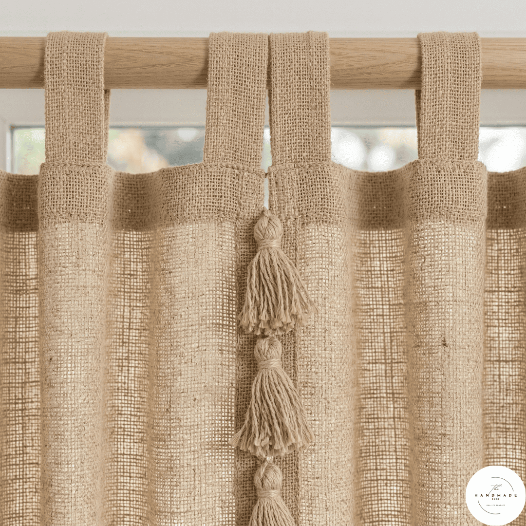 Detail of a textured cream cotton curtain panel showing the artisanal horizontal weave and handcrafted tonal tassels.