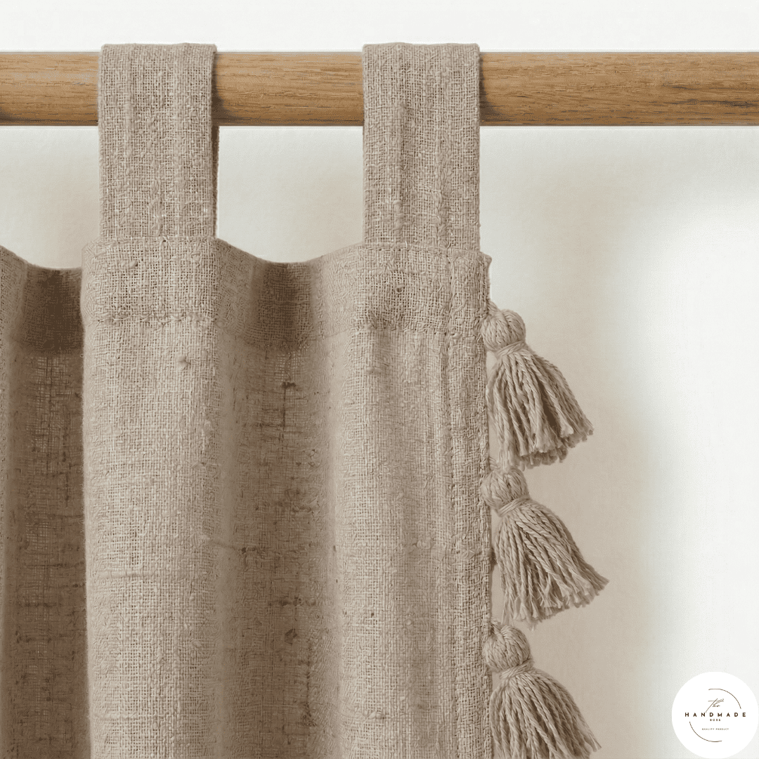 Detail of a textured cream cotton curtain panel showing the artisanal horizontal weave and handcrafted tonal tassels.