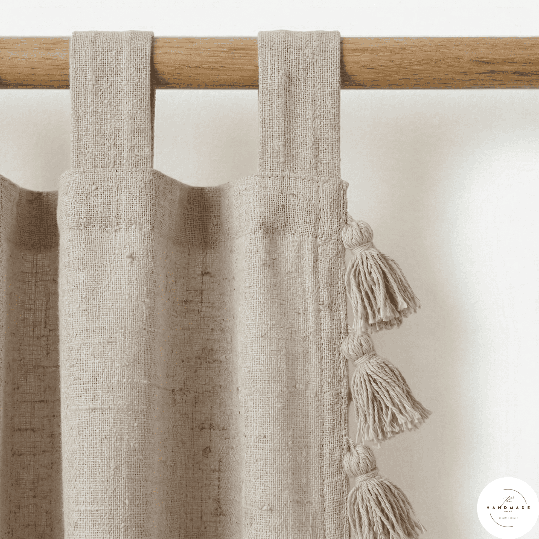Detail of a textured cream cotton curtain panel showing the artisanal horizontal weave and handcrafted tonal tassels.