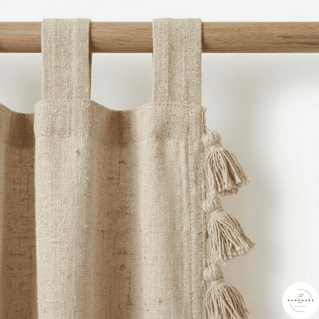 Detail of a textured cream cotton curtain panel showing the artisanal horizontal weave and handcrafted tonal tassels.